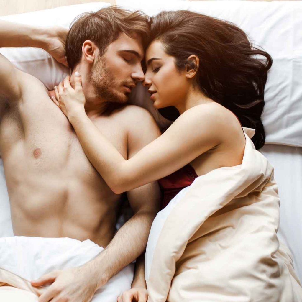 Kærligt par der kysser i sengen under dyne, romantisk intimitet og passion mellem mand og kvinde
