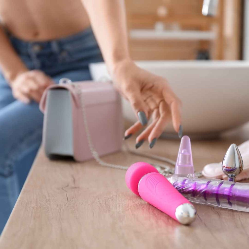Pink vibrator og gennemsigtig dildo på bord foran kvinde med laptop, moderne sexlegetøj til solo leg og diskret opbevaring i hjemmet