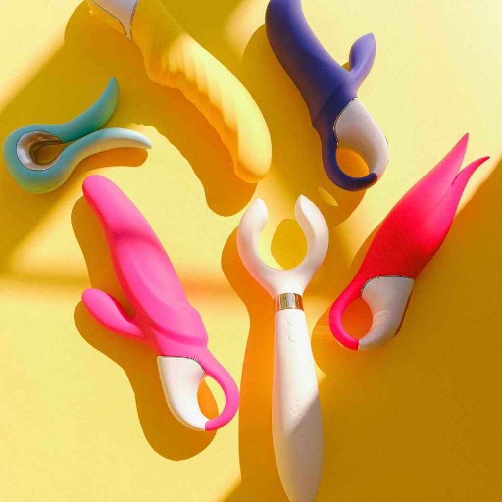 Flere farverige vibratorer og dildoer arrangeret på gul baggrund, sexlegetøj i forskellige former til solo leg og par