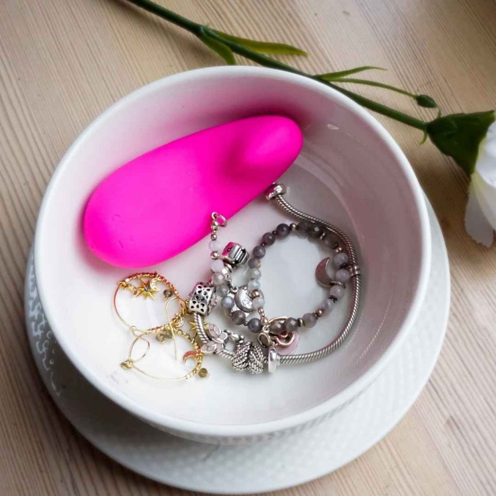 Pink vibrator og sølv anal plug placeret på tallerken med smykker, diskret og elegant sexlegetøj til kvinden