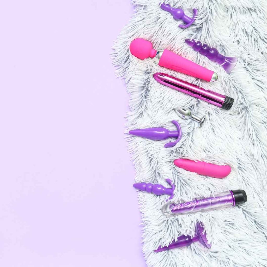 Pink sexlegetøj og kondomer placeret på lyst underlag, vibratorer og beskyttelse til sikker solo leg og parbrug